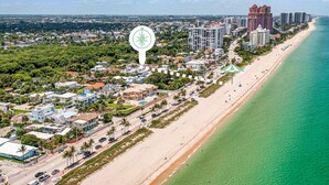An aerial view of a coastal city with a beach, buildings, and a prominent green compass sign.