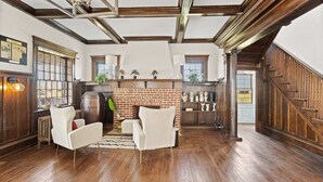 A spacious room with a brick fireplace, wooden beams, and a staircase.
