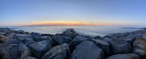 A rocky shoreline with a pier extending into the water, under a clear sky.