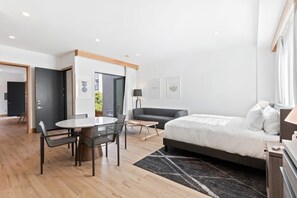 Quarto de hotel moderno com cama, mesa de jantar com cadeiras, um sofá e uma pequena escrivaninha.