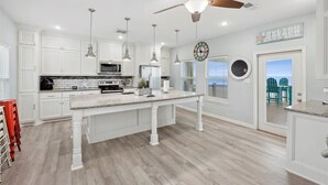 A spacious kitchen with white cabinetry, a large island, pendant lighting, and a ceiling fan. - Shore is Fine - Beachfront, AwesomeViews (Port Bolivar)