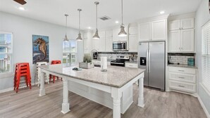 A modern kitchen with white cabinetry, a granite island, stainless steel appliances, and pendant lighting. - Shore is Fine - Beachfront, AwesomeViews (Port Bolivar)