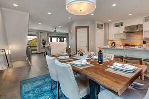 A modern kitchen with white cabinets, a wooden dining table set for four, and a view of the outdoors.