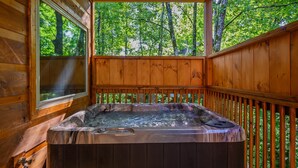 A wooden deck with a hot tub, wooden railings, and a view of a forest. - We love Dogs! Hot Tub, Pool Table, Media Room, Easy Access | Free Tickets! (Pigeon Forge)