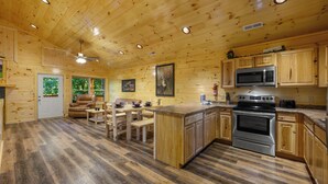 A wooden cabin interior with a kitchen, dining area, and a fireplace. - We love Dogs! Hot Tub, Pool Table, Media Room, Easy Access | Free Tickets! (Pigeon Forge)