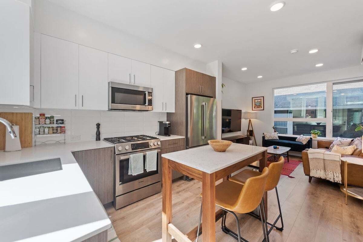 A modern kitchen with white cabinets, stainless steel appliances, and a wooden dining table with bar stools.