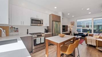 A modern kitchen with white cabinets, stainless steel appliances, and a wooden dining table with bar stools.