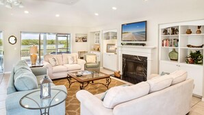 A spacious living room with a fireplace, a television, and a bookshelf. - Three Bedroom Pool Home- Direct Channel Views (Captiva)