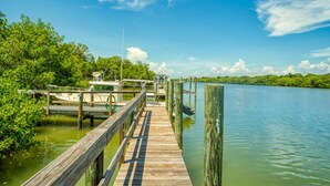A wooden dock extending into a calm body of water, surrounded by lush greenery and a clear blue sky. - Three Bedroom Pool Home- Direct Channel Views (Captiva)
