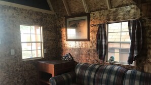 A cozy room with a plaid sofa, a small wooden table, and two windows with curtains. - Hales Hideaway by the City of Rocks (Oakley)