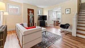 Un salón amplio con un sofá blanco, un televisor de pantalla plana, un piano y una escalera.