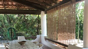 An outdoor patio with a table and chairs, surrounded by a covered area with a wooden ceiling and a woven screen. - Delightful little villa in Vulcan (Sicilia)