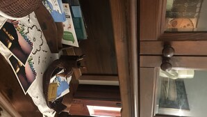 A wooden cabinet with a glass door, a woven basket, and various items including books and a map. - Delightful little villa in Vulcan (Sicilia)