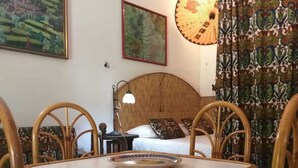 A room with a round table, four chairs, a bed with a wooden headboard, and two paintings on the wall. - Delightful little villa in Vulcan (Sicilia)