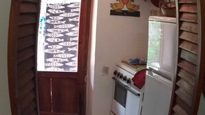 A compact kitchen with a checkered floor, a refrigerator, an oven, and a window with patterned curtains. - Delightful little villa in Vulcan (Sicilia)