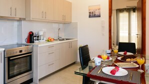 Een moderne keuken met een ingebouwde oven, een koffiezetapparaat en een spoelbak. Er staat een eettafel gedekt met borden, glazen en een stoel.