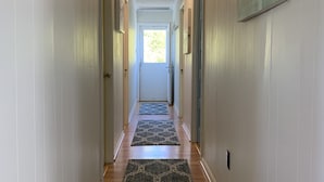 Un pasillo con piso de madera, paredes blancas y dos alfombras que conducen a una puerta.