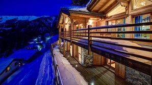A wooden cabin with a stone foundation, a wooden deck, and a view of snow-covered mountains. - Chalet Auriane - Five Bedroom Chalet, Sleeps 12 (Riddes)