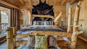 A log cabin bedroom with a bed centered on a wooden frame, flanked by wooden walls and a large window. - Chalet Auriane - Five Bedroom Chalet, Sleeps 12 (Riddes)