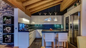A modern kitchen with a stone wall, wooden ceiling beams, and stainless steel appliances. - Chalet Auriane - Five Bedroom Chalet, Sleeps 12 (Riddes)