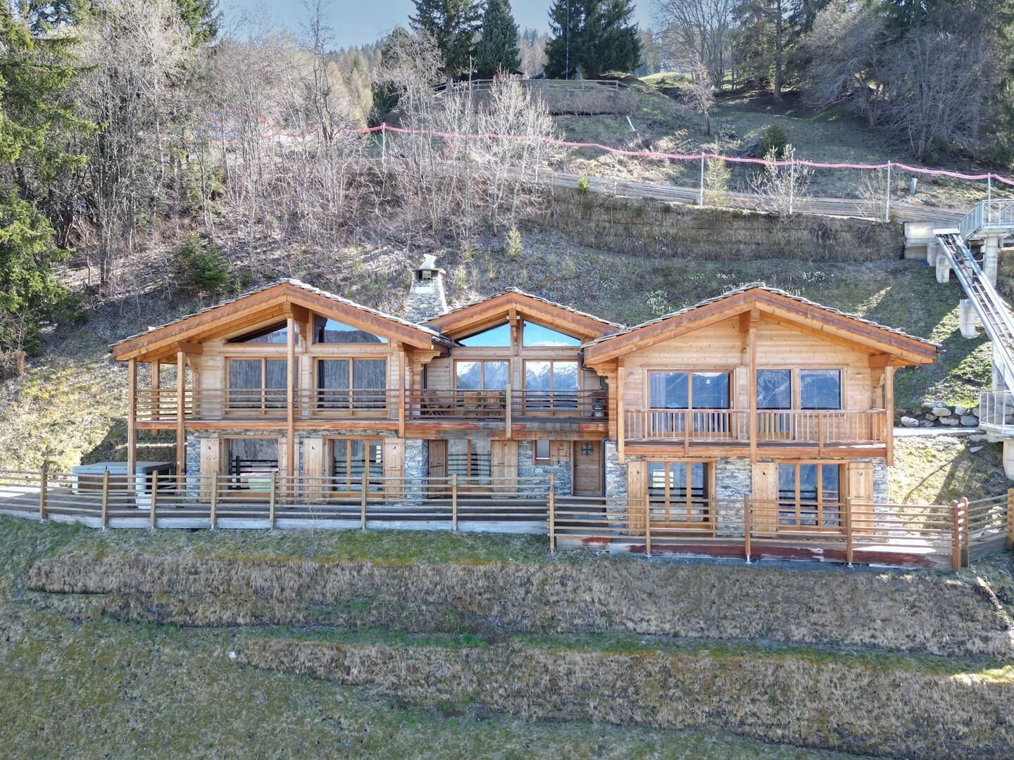 Een houten chalet met meerdere balkons en grote ramen, gelegen op een heuvel met uitzicht op het omliggende landschap.