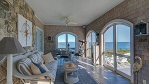 A sunlit room with a stone wall, a striped sofa, a telescope, and a view of the ocean.