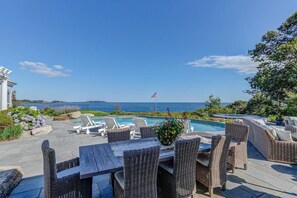 A pool area with lounge chairs, a flag, and a view of the sea.