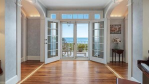 A spacious room with a wooden floor, large glass doors leading to a balcony with a view of the sea.