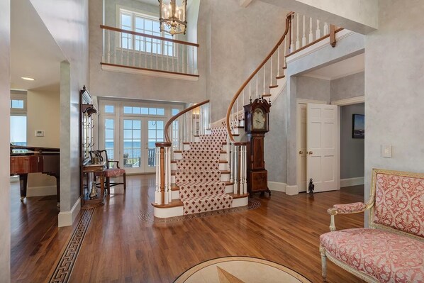 Un intérieur spacieux avec un grand escalier, un coin repas et une vue sur l’extérieur.