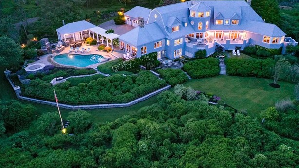 A large, multi-story house with a swimming pool, surrounded by lush greenery.