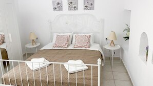 A bedroom with a white metal bed frame, a beige bedspread, two decorative pillows, a white headboard, and three wall-mounted flower paintings.