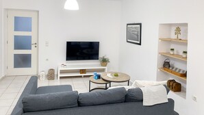 A modern living room with a grey sofa, a flat-screen TV, a small round table with a plant, and a bookshelf with decorative items.
