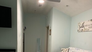 A bedroom with two beds, a ceiling fan, a wall with a motivational quote, and a hallway leading to another room.