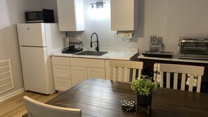 A compact kitchen with white cabinets, a white refrigerator, a sink, a microwave, a toaster, and a dining table with chairs.