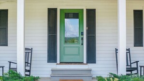 A front porch with a green door, white siding, and black shutters.