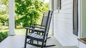 A rocking chair on a porch with a white exterior wall and a green lawn in the background.