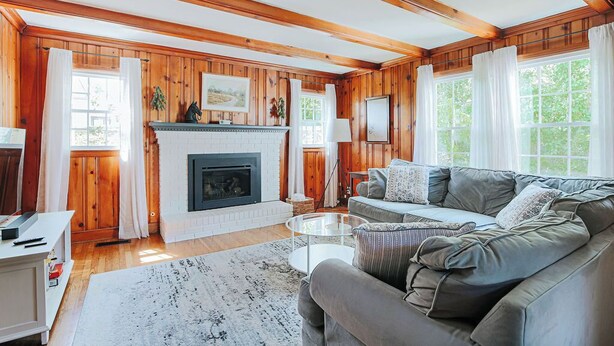 A cozy living room with wooden paneling, a fireplace, a grey sofa, and a round coffee table.