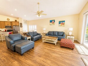 A spacious living area with a kitchen, a ceiling fan, and artwork on the walls. - Lovely Pool Home With Spa & Games Room Close to WDW (Clermont)