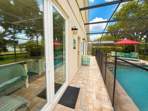 A poolside area with a glass door leading to a pool, outdoor furniture, and a pergola with umbrellas. - Lovely Pool Home With Spa & Games Room Close to WDW (Clermont)