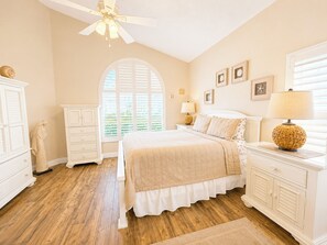 A bedroom with a bed, nightstands, a dresser, a ceiling fan, and a window with shutters. - Lovely Pool Home With Spa & Games Room Close to WDW (Clermont)