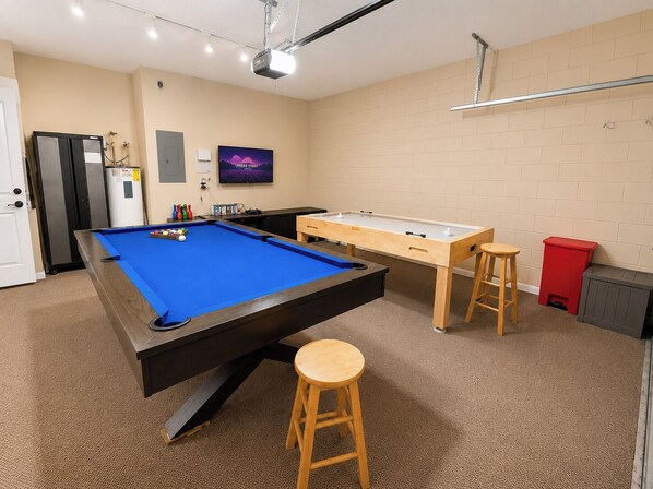 A pool table with stools, a projector, and a ping pong table in a room with beige walls and carpet. - Lovely Pool Home With Spa & Games Room Close to WDW (Clermont)
