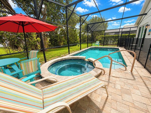 A covered outdoor swimming pool with lounge chairs and a red umbrella.
