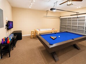 A pool table with a blue felt surface, a foosball table, and a television displaying 'GAME ROOM' in a room with beige walls and carpet. - Lovely Pool Home With Spa & Games Room Close to WDW (Clermont)