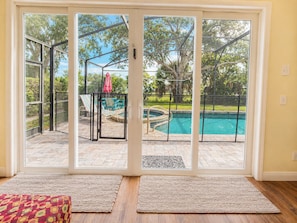 A room with a sliding glass door leading to an outdoor pool area with a view of trees and a red umbrella.