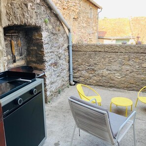 An outdoor kitchen area with a stone wall, a grill, and yellow chairs.