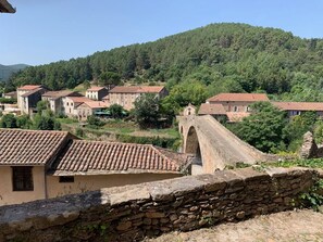 Un village rural avec des bâtiments en pierre, un pont et une colline.
