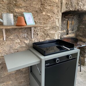 Un réchaud portatif doté d’une surface de cuisson plane, d’une table d’appoint et, en arrière-plan, d’un mur en pierre rustique.