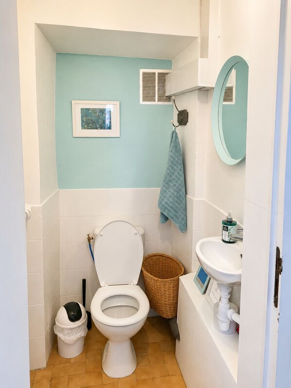 A compact bathroom with a toilet, a sink, a framed picture on the wall, and a basket.