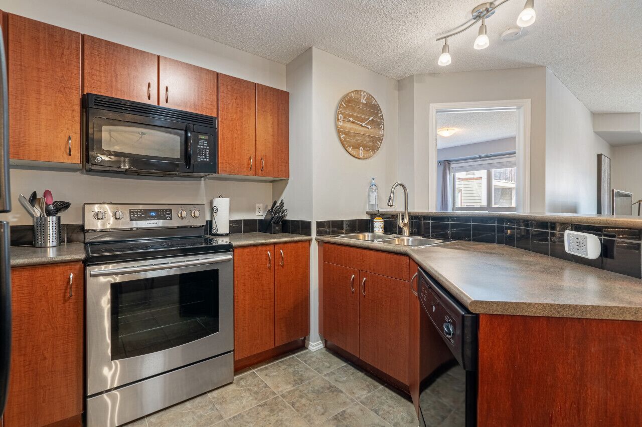 A modern kitchen with wooden cabinets, stainless steel appliances, and a large clock on the wall.