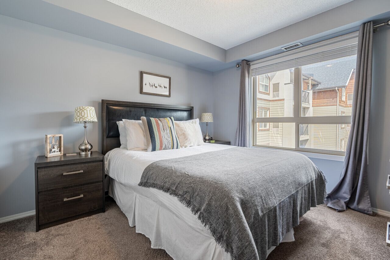 A bedroom with a large bed, two bedside tables, a window with curtains, and a framed picture on the wall.
